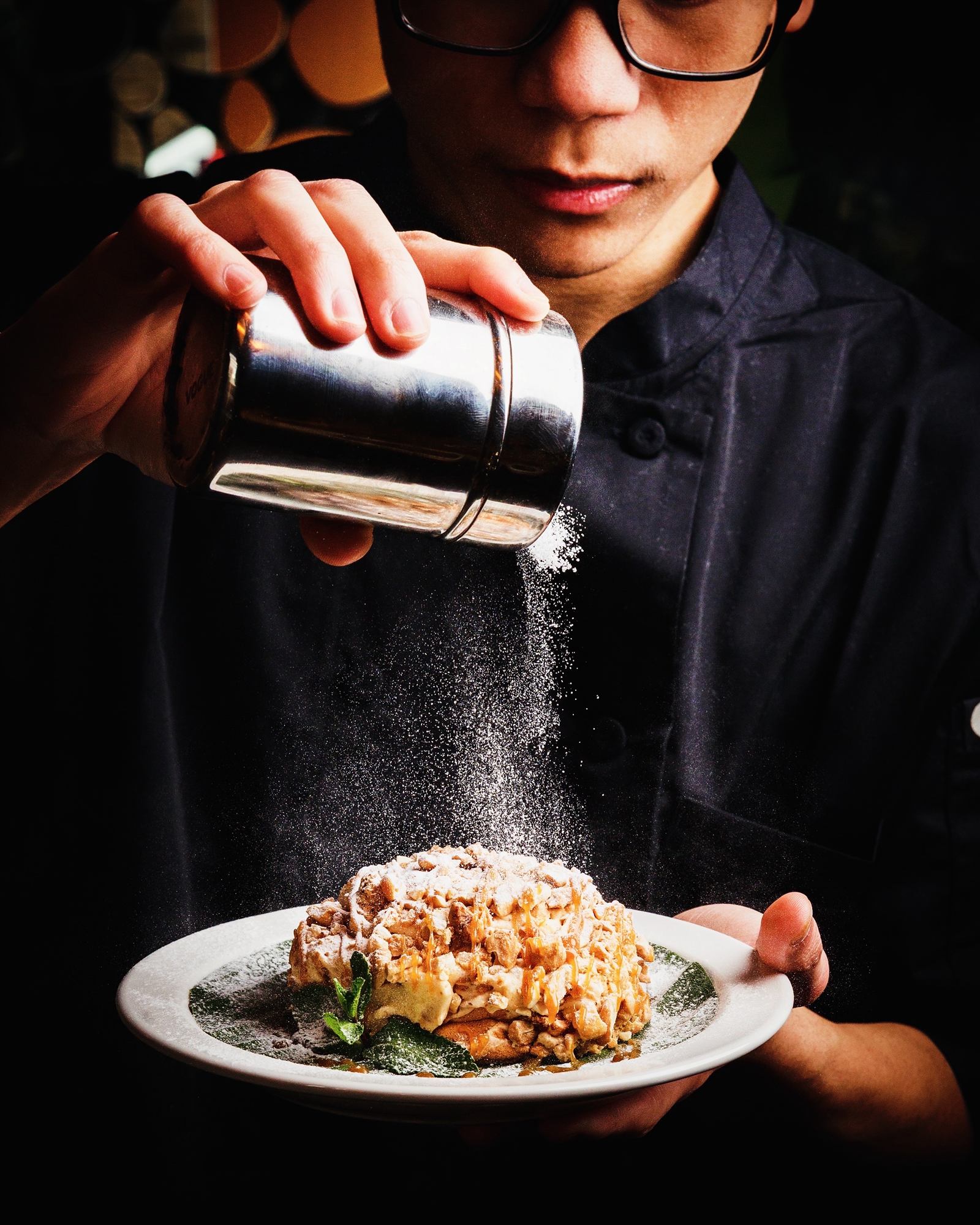 Chef dusting icing sugar over a plated dessert at Mina's Table