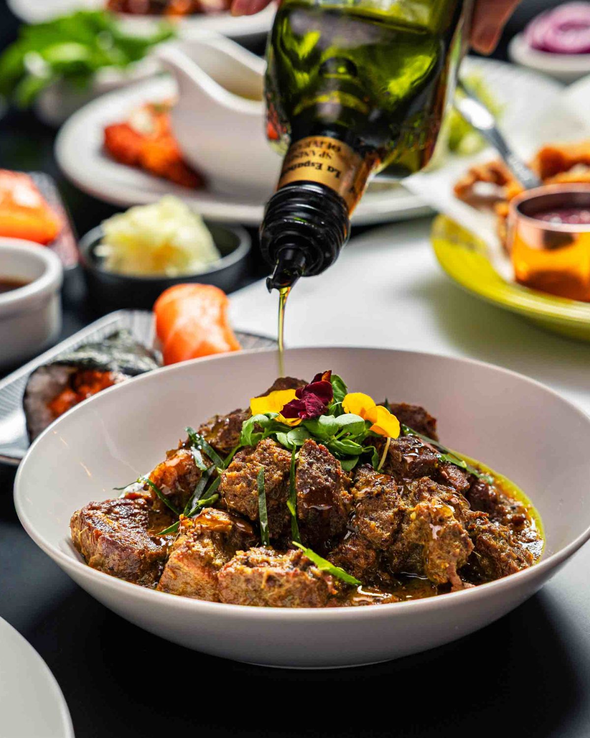 A weekend sharing feast at Mina's Table — a bowl of beef rendang finished with herb oil amid a spread of dishes