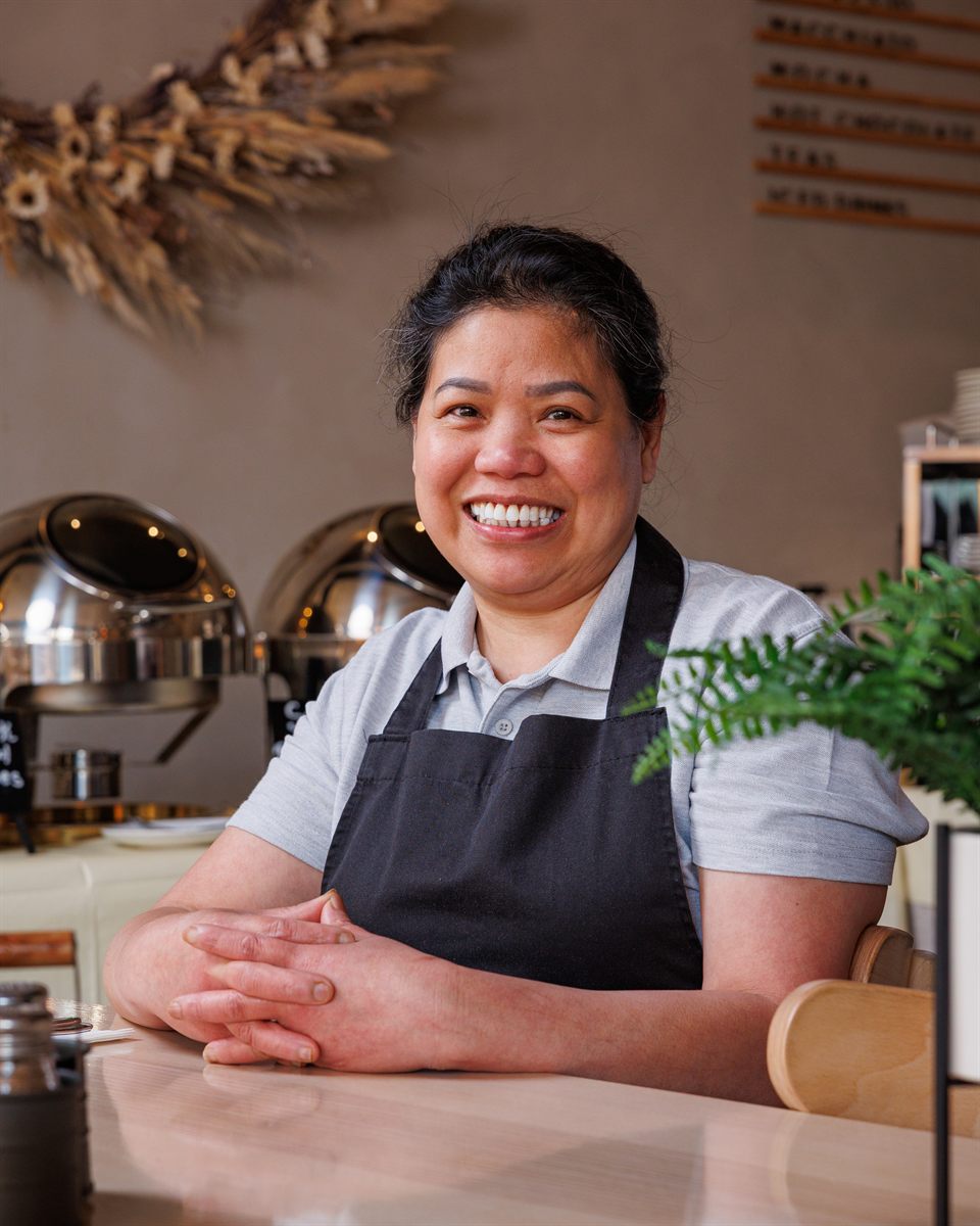 Mina in her apron at the pass, smiling in the Mina's Table dining room