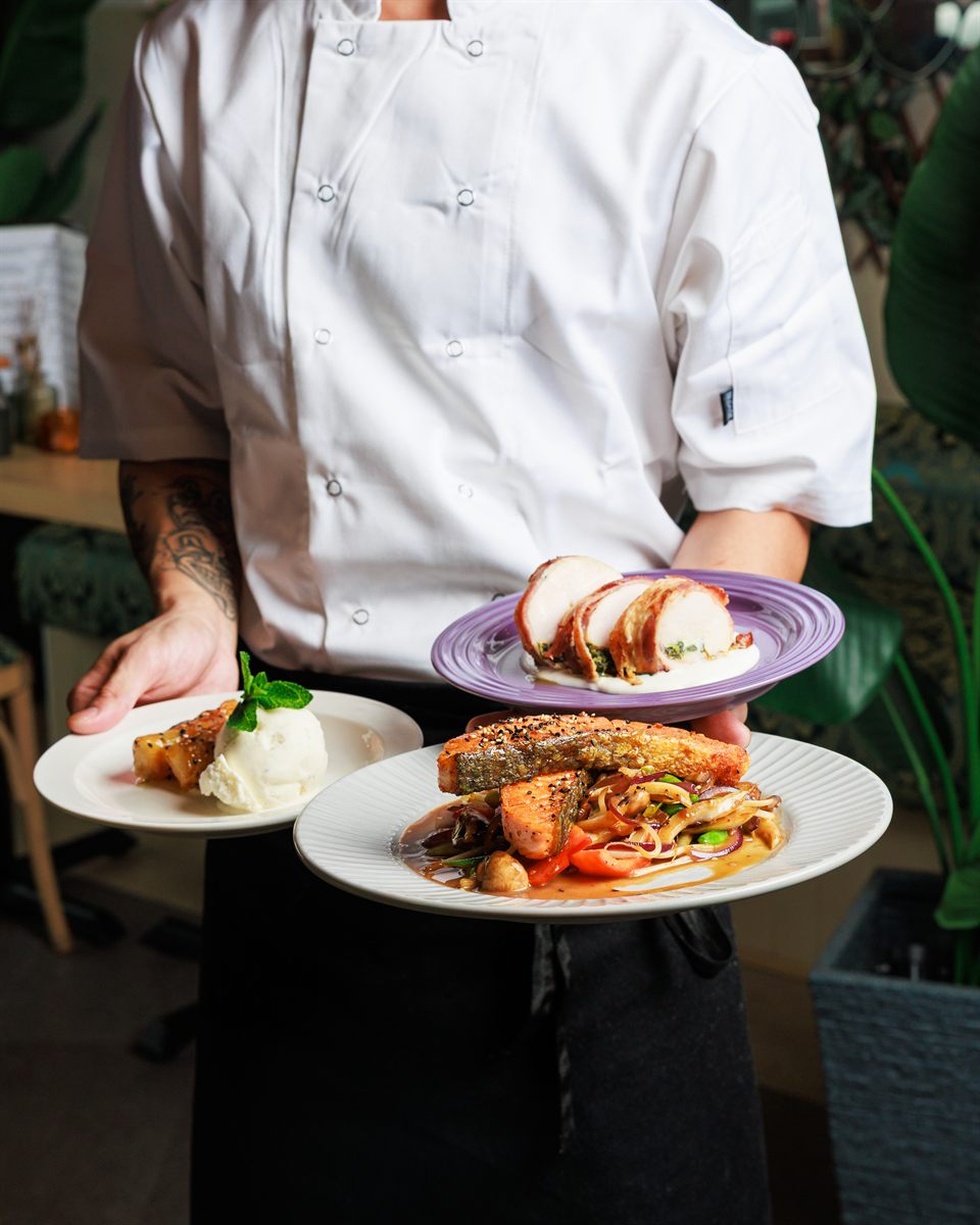 A chef carrying three plated dishes out to the dining room during service