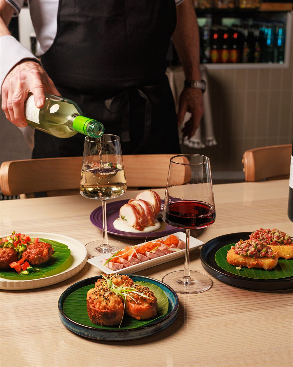 White wine poured at a table laid with small plates at Mina's Table