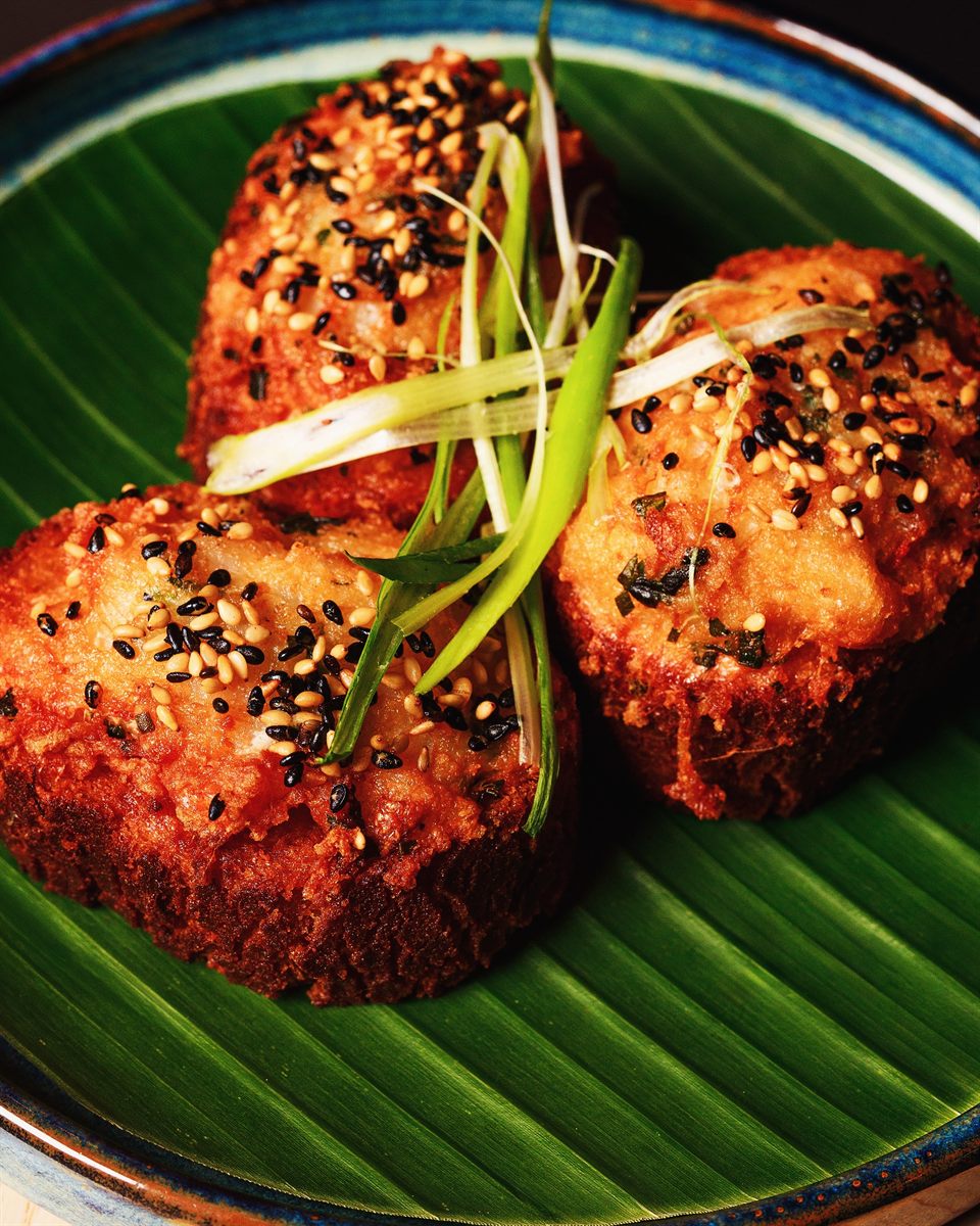 Close-up of sesame-crusted golden bites finished with spring onion on a banana leaf