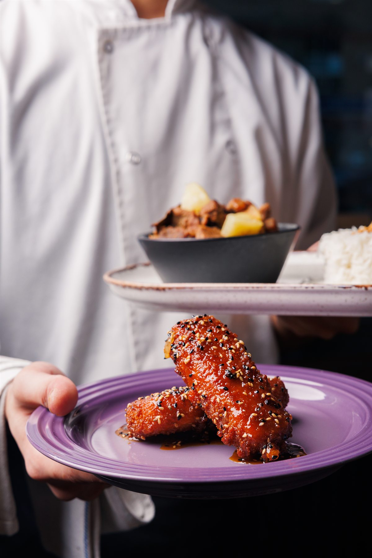 A chef presenting sesame-glazed mozzarella alongside other dishes at Mina's Table